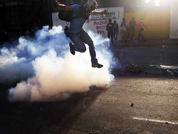 Manifestante salta em meio à fumaça do gás lacrimogêneo. (Foto: Rodrigo Abd / AP Photo)