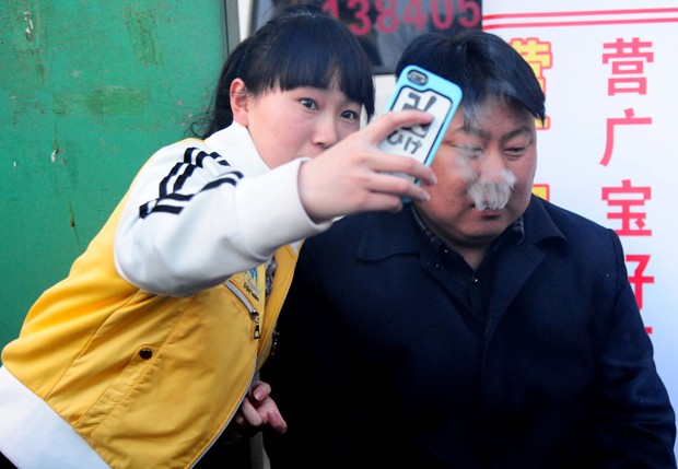 Mulher faz 'selfie' ao lado de vendedor de churrasco na China (Foto: STR/AFP)