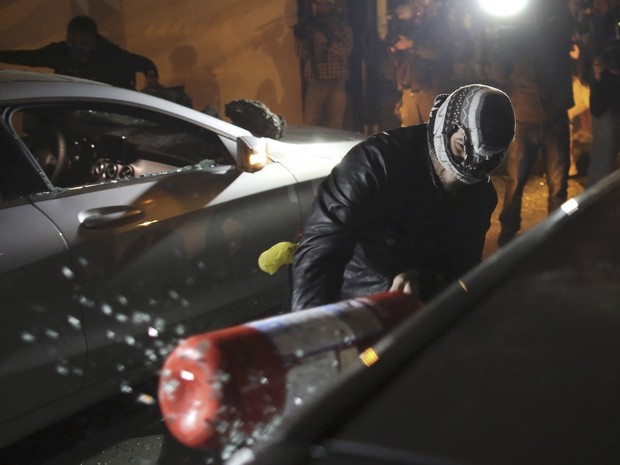 Mascarado usa extintor de incêndio para quebrar a janela de um veículo dentro de concessionária na Marginal Pinheiros, em São Paulo, durante protesto (Foto: Nacho Doce/Reuters)