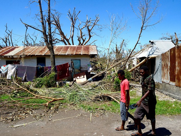 Moradores passam por uma casa danificada pelo ciclone 'Pam' na ilha de Tanna, em Vanuatu. As ilhas mais afetadas pelo fenômeno começaram a receber ajuda nesta quarta-feira (18), enquanto outras continuam isoladas (Foto: Jeremy Piper/AFP)