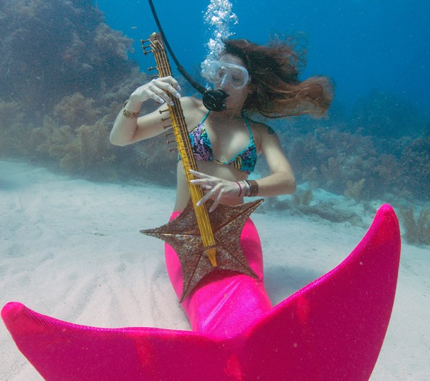 Vestida de sereia, Sarah Brunner finge tocar uma guitarra de estrela-do-mar no festival de música (Foto: Reuters)