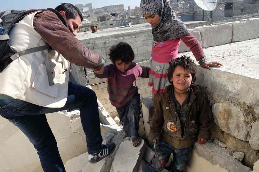 Crianças mostram casa para um dos funcionários da ONG que as resgatou (Foto: Nicholson/Caritas)