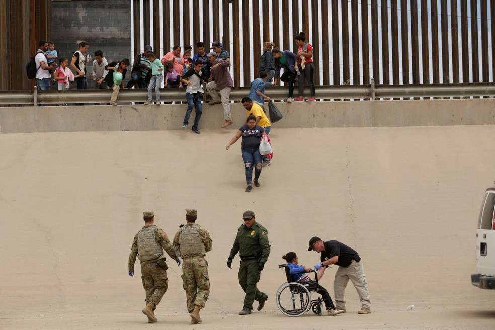 Agentes da patrulha de fronteira e membros das forças armadas americanas ajudam uma mulher migrante em uma cadeira de rodas depois que ela e outras pessoas atravessaram ilegalmente a fronteira entre EUA e México em El Paso, no Texas, para pedir asilo — Foto: Jose Luis Gonzalez/Reuters