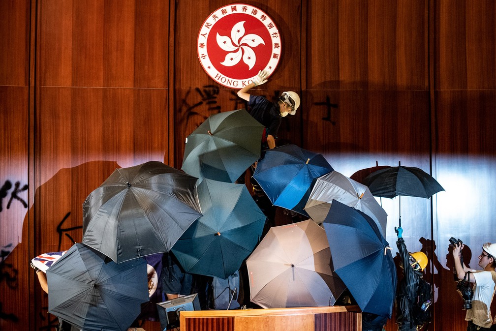 1º de julho - Manifestantes vandalizam o emblema de Hong Kong após cercarem e invadirem o Parlamento da região semiautônoma, no dia do aniversário de 22 anos da entrega da cidade do Reino Unido para a China. Uma forte onda de manifestações tomou Hong Kong no 2º semestre após um projeto de lei que autoriza a extradição de moradores à China continental — Foto: Philip Fong/AFP