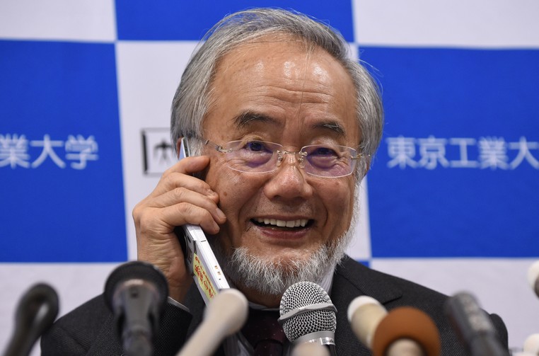   Yoshinori Ohsumi sorri ao falar pelo telefone com o primeiro-ministro Shinzo Abe durante coletiva de imprensa em Tóquio, no Japão, após anúncio de que que ele havia sido laureado com o Prêmio Nobel (Foto: Toru Yamanaka/AFP)