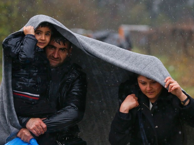 Migrantes se protegem da chuva com um cobertor durante caminhada para atravessar a fronteira da Grécia com a Macedônia (Foto: Stoyan Nenov/ Reuters)