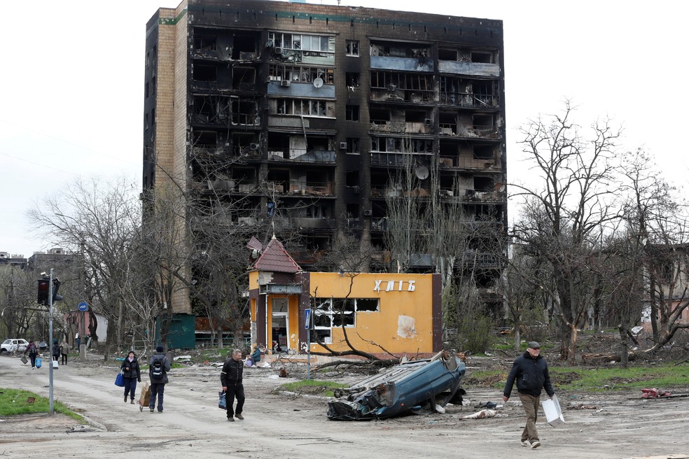 Pessoas caminham em frente a prédio residencial fortemente danificado durante conflito entre Rússia e Ucrânia na cidade ucraniana de Mariupol — Foto: Alexander Ermochenko/REUTERS