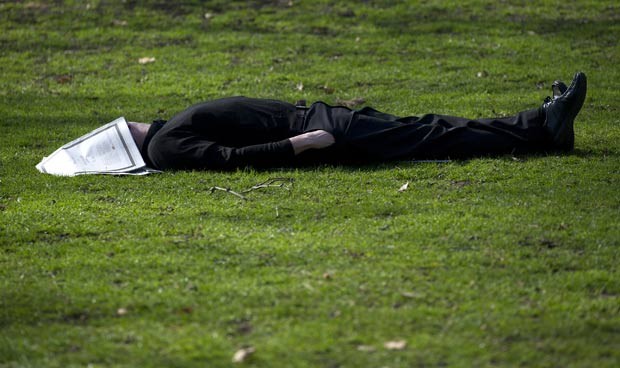 Com jornal como máscara, homem tira soneca em parque. (Foto: Carl Court/AFP)