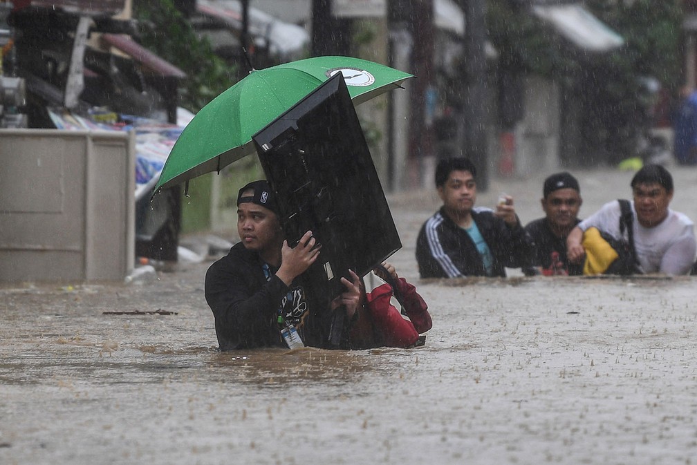 Homem carrega televisão enquanto atravessa rua inundada, nesta quinta-feira (12), depois que o Tufão Vamco atingiu a cidade de Marikina City, nas Filipinas. — Foto: Ted Aljibe/AFP