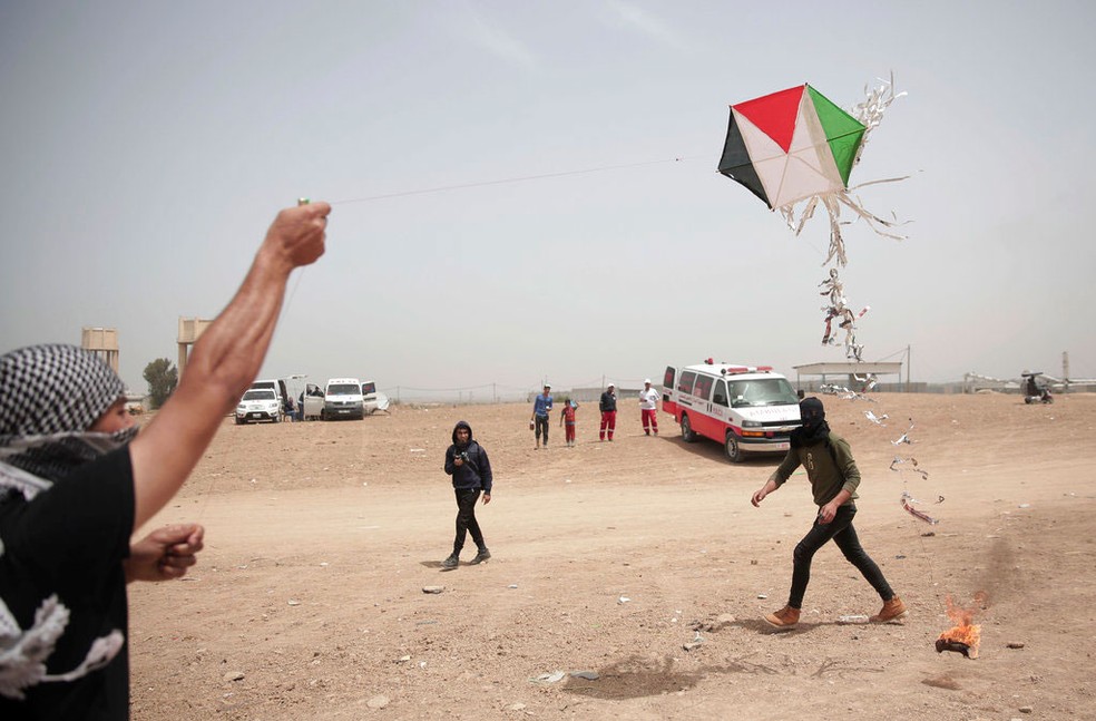 Manifestantes palestinos empinam uma pipa com um pano em chamas pendurado durante protesto na fronteira da Faixa de Gaza com Israel, nesta sexta-feira (20)   (Foto: Khalil Hamra/ AP)