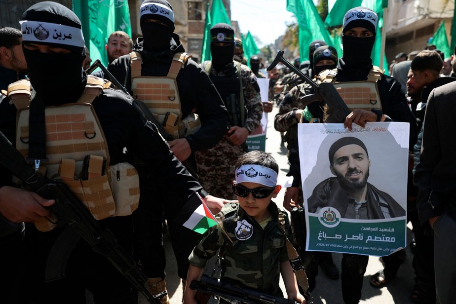 Criança e integrantes do braço militar do Hamas usam faixas do Toca do Leão durante protesto para denunciar a morte de palestinos por soldados israelenses