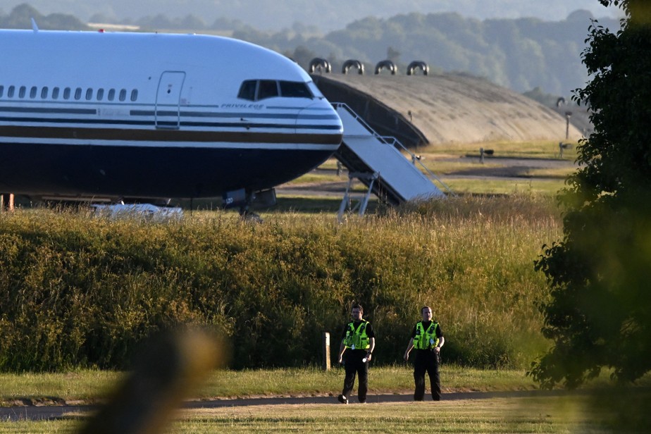 Policiais caminham perto de onde um Boeing 767 na pista da base militar de Amesbury, Salisbury, onde se preparava para enviar refugiados do Reino Unido para Ruanda