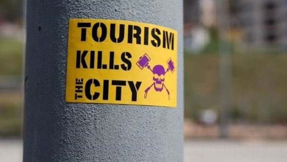 'O turismo mata a cidade', diz um adesivo colado em um poste, em Barcelona — Foto: Getty Images via BBC