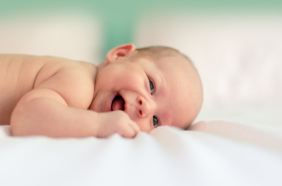 Bebê sorri deitado em lençol  — Foto: Unsplash