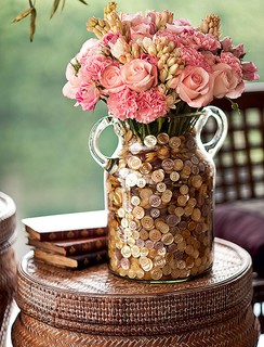 Dentro da ânfora, um vaso menor com água acomoda rosas, cravos e angélicas, camuflados no farto punhado de botões de madrepérola