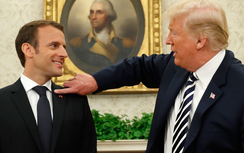 O presidente dos EUA, Donald Trump, limpa o ombro do presidente francês, Emmanuel Macron, durante encontro na Casa Branca, na terça-feira (24) (Foto: Reuters/Kevin Lamarque)