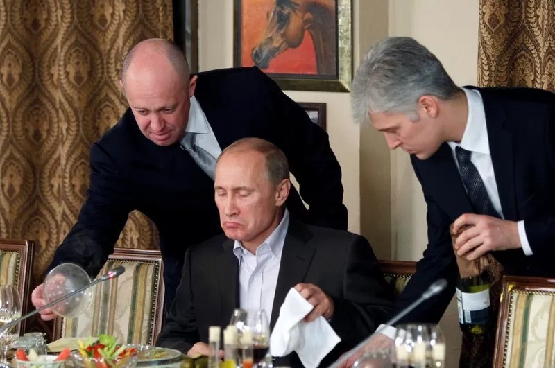 Uma foto de novembro de 2011 mostra Yevgeny Prigozhin (E) auxiliando Vladimir Putin em um banquete perto de Moscou (Foto: Reuters via BBC News Brasil)