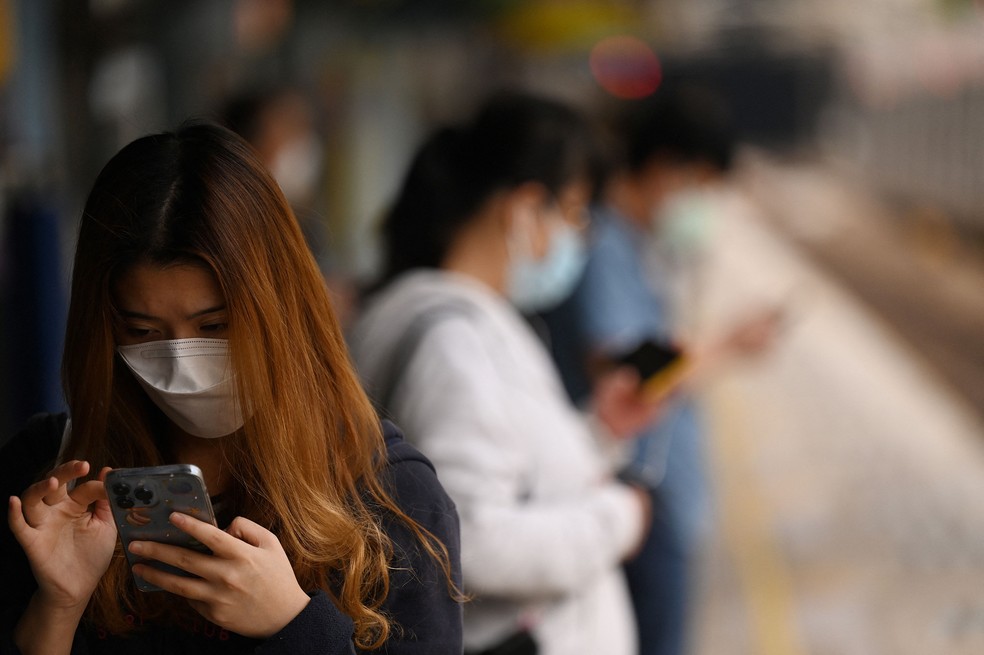 Mulher usa máscara enquanto mexe no celular em plataforma de trem de Hong Kong, em 6 de março de 2022. — Foto: Peter Parks / AFP