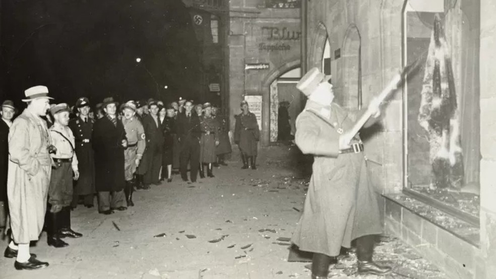 Pessoas observam oficial nazista atacar loja de um judeu — Foto: YAD VASHEM PHOTO ARCHIVE via BBC