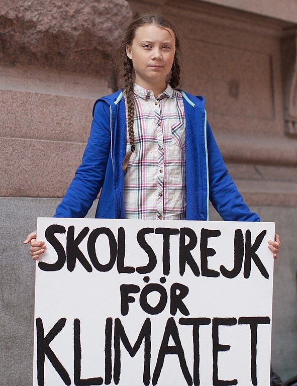 Greta Thunberg segurando uma placa de protesto escrita 
