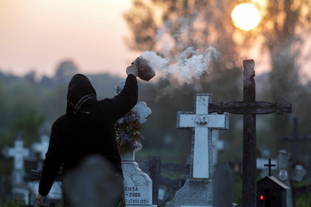 25 de abril - Uma mulher queima incenso perto do túmulo de parentes em um cemitério a 50 quilômetros a sudoeste de Bucareste, na Romênia. Cristãos ortodoxos de pequenas aldeias locais vão aos cemitérios durante o amanhecer como parte de um ritual centenário da Semana Santa em que levam velas, acendem incensos e deixam pequenos sacos de comida  — Foto: Octav Ganea/Iquam/via Reuters