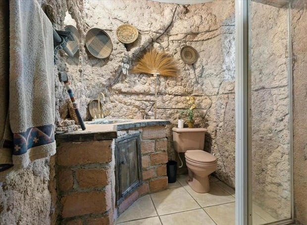 Banheiro com decoração que inclui artefatos indígenas e outras estranhezas, com parede com textura de pedra rústica (Foto: Zillow Gone Wild / Reprodução)