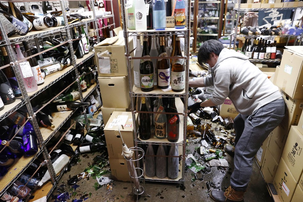 13 de fevereiro - Homem limpa garrafas quebradas em uma loja de bebidas após um forte terremoto em Fukushima, no Japão. — Foto: Kyodo/via Reuters