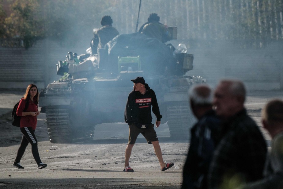 Pessoas atravessam a rua atrás de um tanque ucraniano na recém-recuperada cidade de Kupiansk