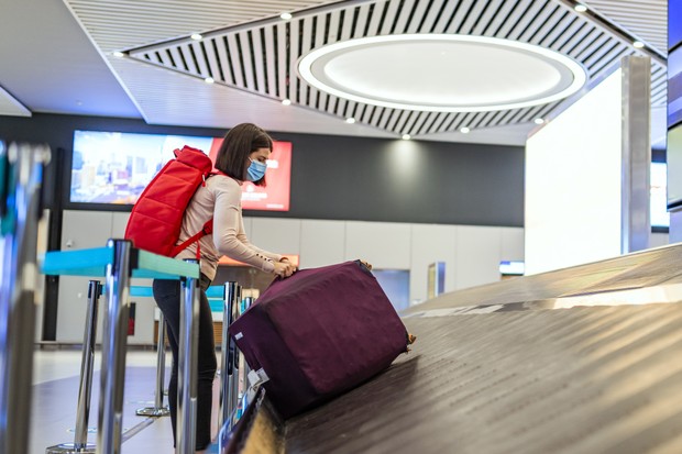 Young woman picking luggage from conveyor belt in airport (Foto: Getty Images)