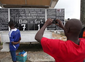 Pessoas passam para olhar notícias sobre o Ebola na capital da Libéria (Foto: Agência EFE)