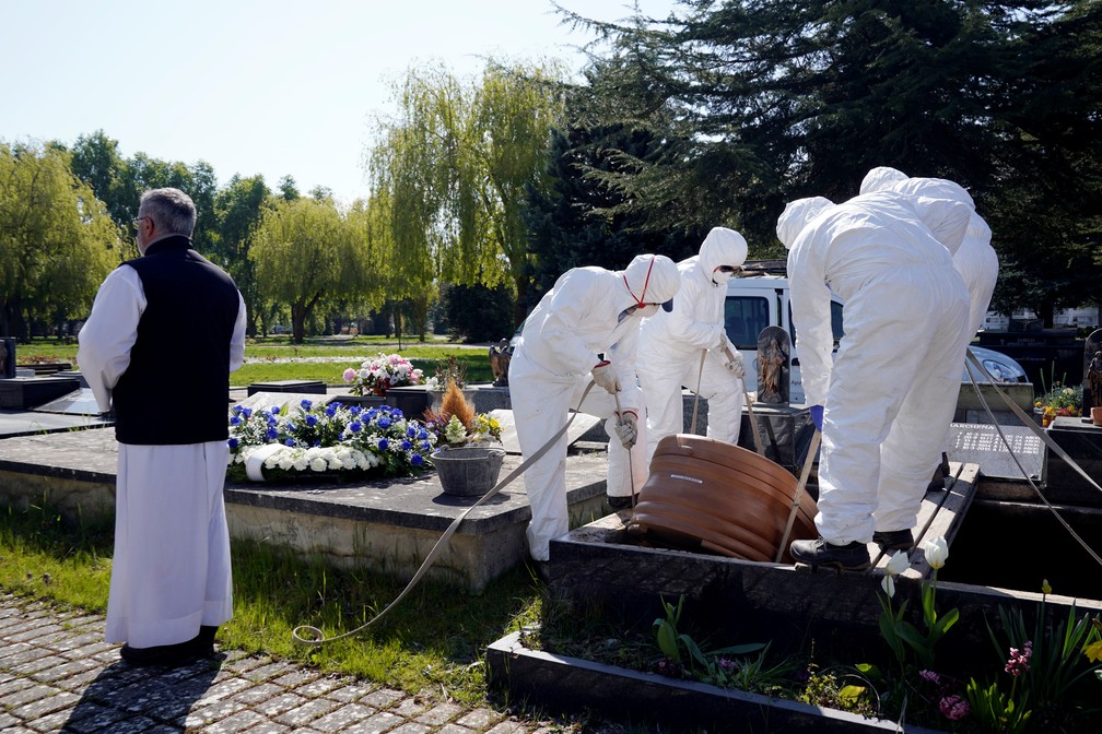 Funcionários do cemitério El Salvador usam roupas de proteção em enterro de vítima do novo coronavírus na Espanha — Foto: Vincent West/Reuters