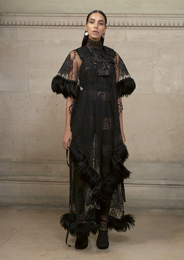 Lea T wears an embroidered illusion-tulle dress with delicate geometric floral motifs, trimmed with ribbons of black rooster feathers. At the chest is a cut-and-glued feathered front worn with an encrusted-lace jersey jumpsuit (Foto: Givenchy)