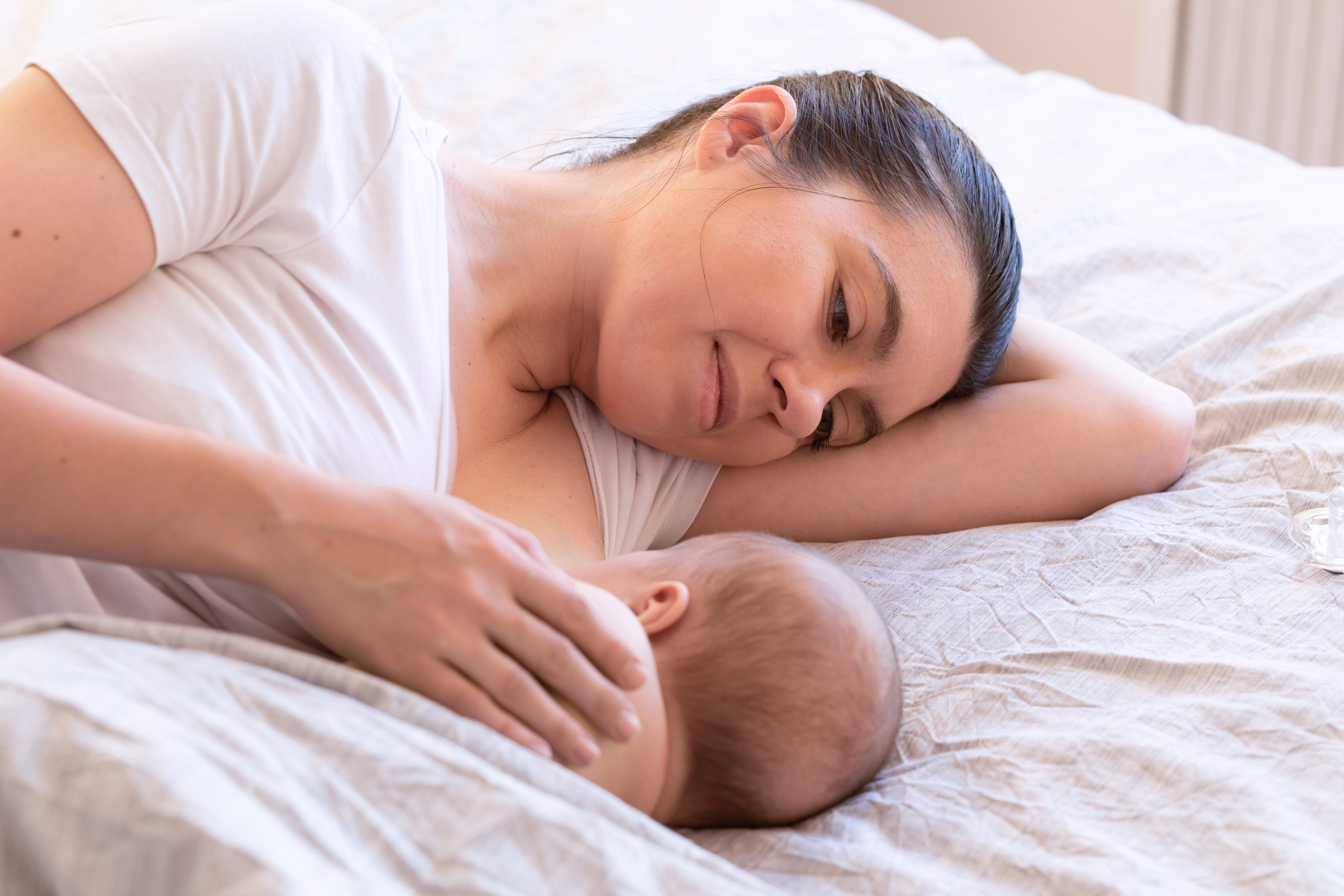 Mãe amamentando bebê deitada na cama (Foto: Getty Images)