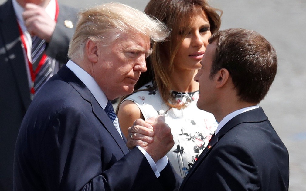 Os presidentes dos EUA e da França, Donald Trump e Emmanuel Macron, se cumprimentam durante a parada militar do Dia da Bastilha, em Paris, na sexta-feira (14), sob o olhar da primeira-dama americana Melania Trump (Foto: Reuters/Yves Herman)