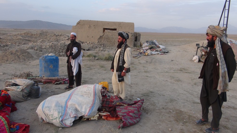 Homens observam cena de ataque que matou 13 pessoas da mesma família no Afeganistão (Foto: FARIDULLAH AHMADZAI / AFP)