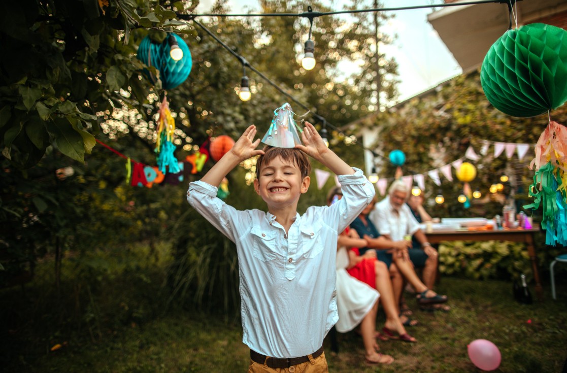 Criança sorridente em festa de aniversário segurando chapéu com as duas mãos (Foto: Getty Images)