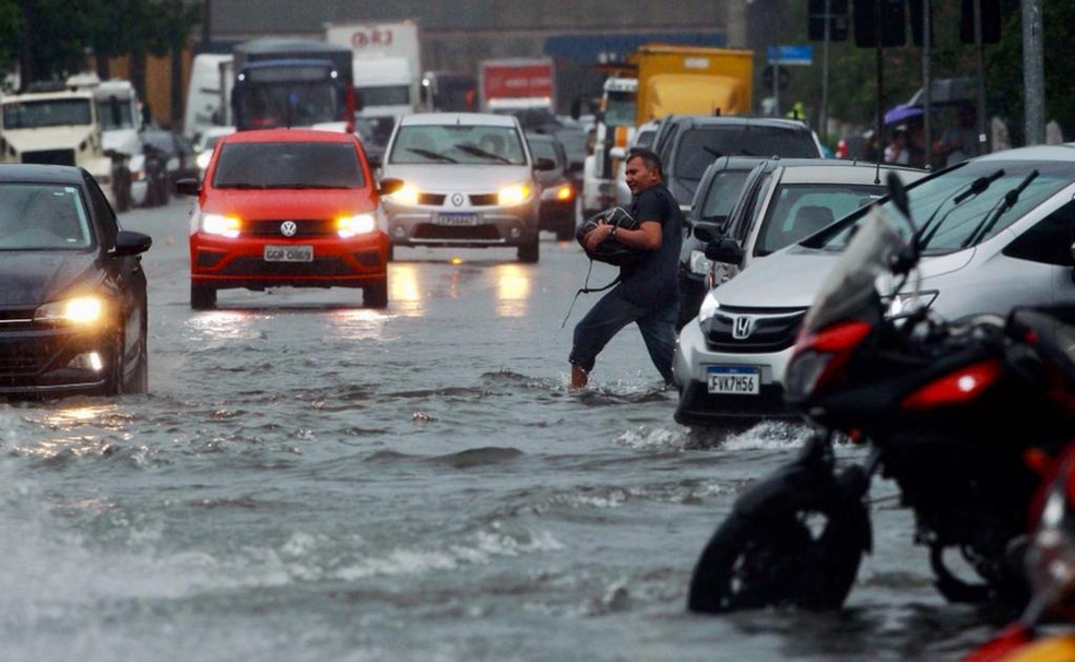 Moradores de Santos que se arriscam na chuva precisam colocar o pé na água para se deslocar — Foto: Vanessa Rodrigues/A Tribuna Jornal