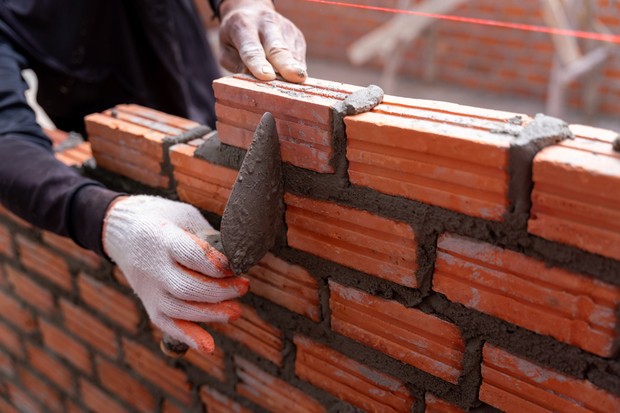 Close up hand of bricklayer worker installing bricks on construction site (Foto: Getty Images)