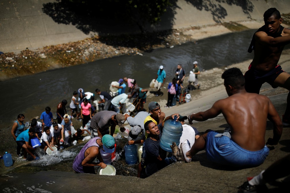 Moradores coletam esgoto no rio guaire, em Caracas, por não terem água em suas casas — Foto: Retuers/Carlos Garcia Rawlins