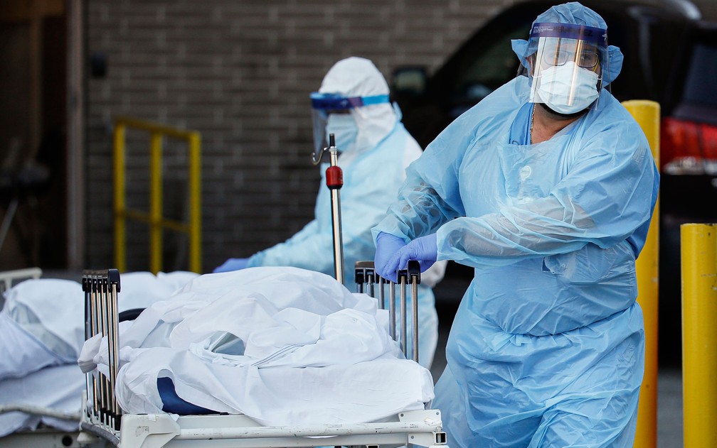 Equipes usam roupas protetoras para transportar corpos de vítimas do coronavírus em NY — Foto: John Minchillo/AP Photo
