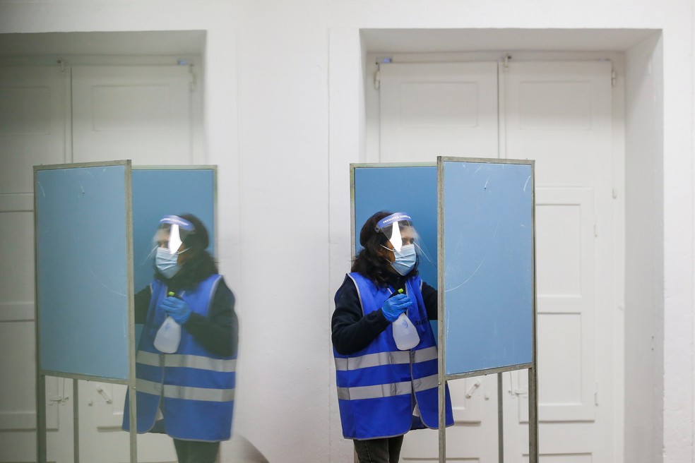 Mulher com máscara protetora e protetor facial limpa cabine de votação em seção eleitoral de LIsboa — Foto: Pedro Nunes/Reuters