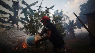 Rosalino de Oliveira joga água tentando proteger sua casa enquanto o fogo se aproxima em uma área da floresta amazônica, perto de Porto Velho, RondôniaREUTERS