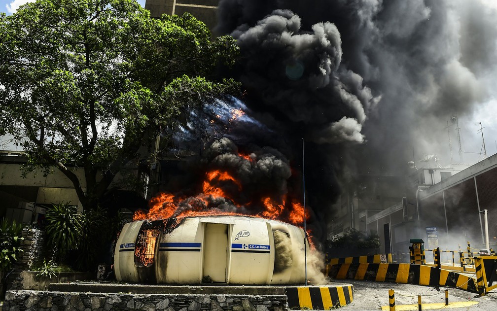 Uma cabine de polícia em chamas é vista em rua de Caracas, na Venezuela, na quinta-feira (20) (Foto: Ronaldo Schemidt/AFP)