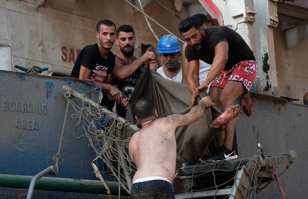 Homens ajudam a retirar marinheiro ferido de navio em porto de Beirute.  — Foto: Hussein Malla/AP Photo
