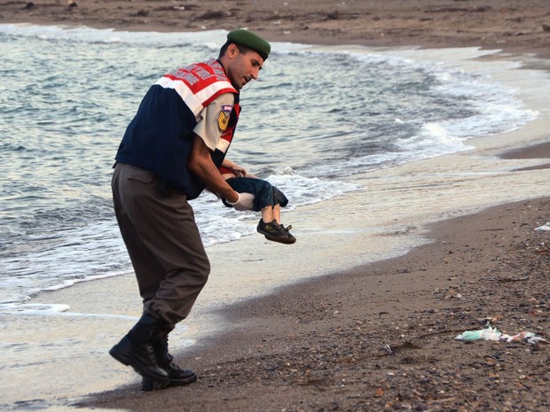 Policial paramilitar recolhe o corpo de uma criança morta que apareceu em praia da ilha de Kos, na Grécia. Vários migrantes morreram afogados e alguns seguem desaparecidos após botes lotados naufragarem durante tentativa de chegar ao território grego (Foto: AP/DHA)