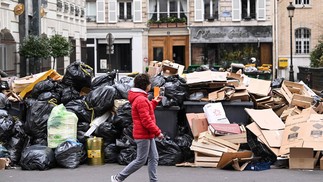 Pedestre passa por um monte de lixo acumulado em uma rua de Paris, durante greve contra a reforma previdenciária proposta pelo governo francês — Foto: Stefano RELLANDINI / AFP