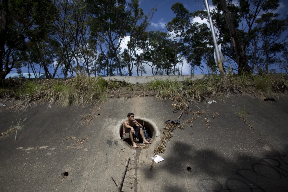 Sentado numa saída de água pluvial, David Garcia, de 19 anos, fuma um cigarro num intervalo enquanto procurava objetos de valor no poluído Rio Guaire, em Caracas. Ele é pai de uma criança de 6 meses (Foto: Ariana Cubillos/AP)