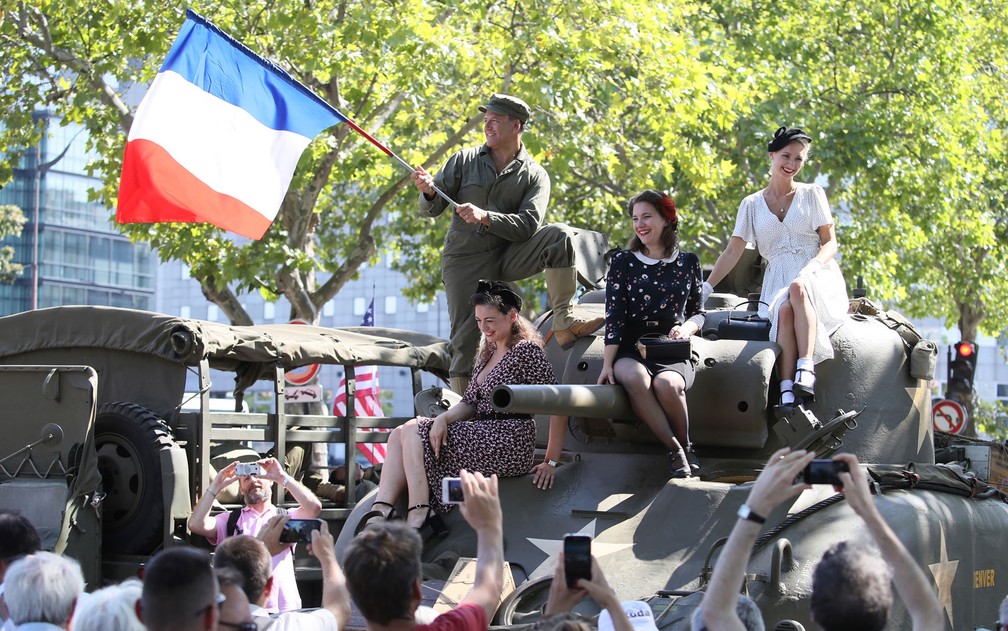 Pessoas vestidas com roupas da época da II Guerra Mundial acenam durante as comemorações dos 75 anos da liberação de Paris da ocupação nazista, no domingo (25) — Foto: AP Photo/David Vincent
