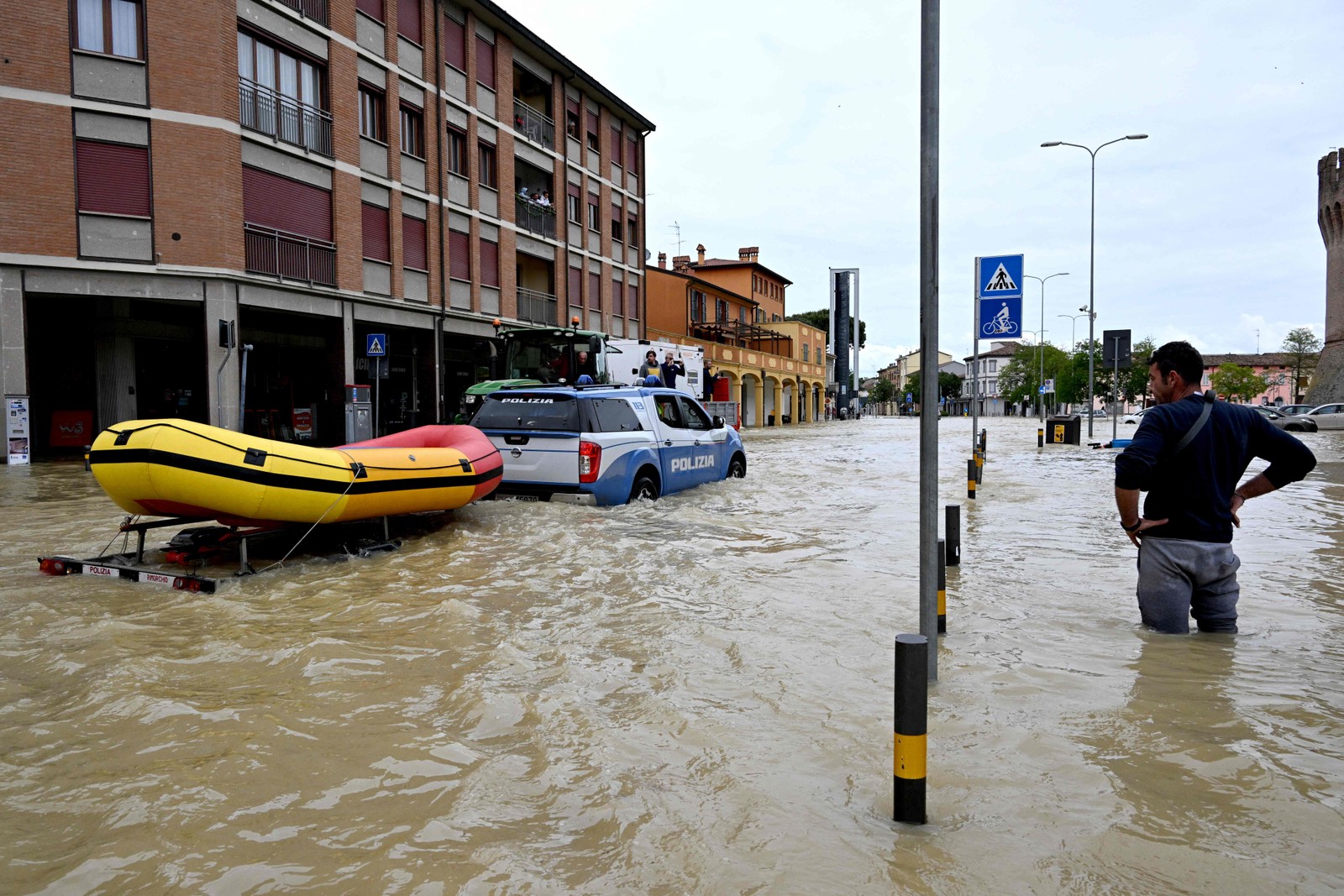 Homem observa carro da polícia que transporta um bote em uma rua inundada na cidade de Lugo — Foto: Andreas SOLARO / AFP