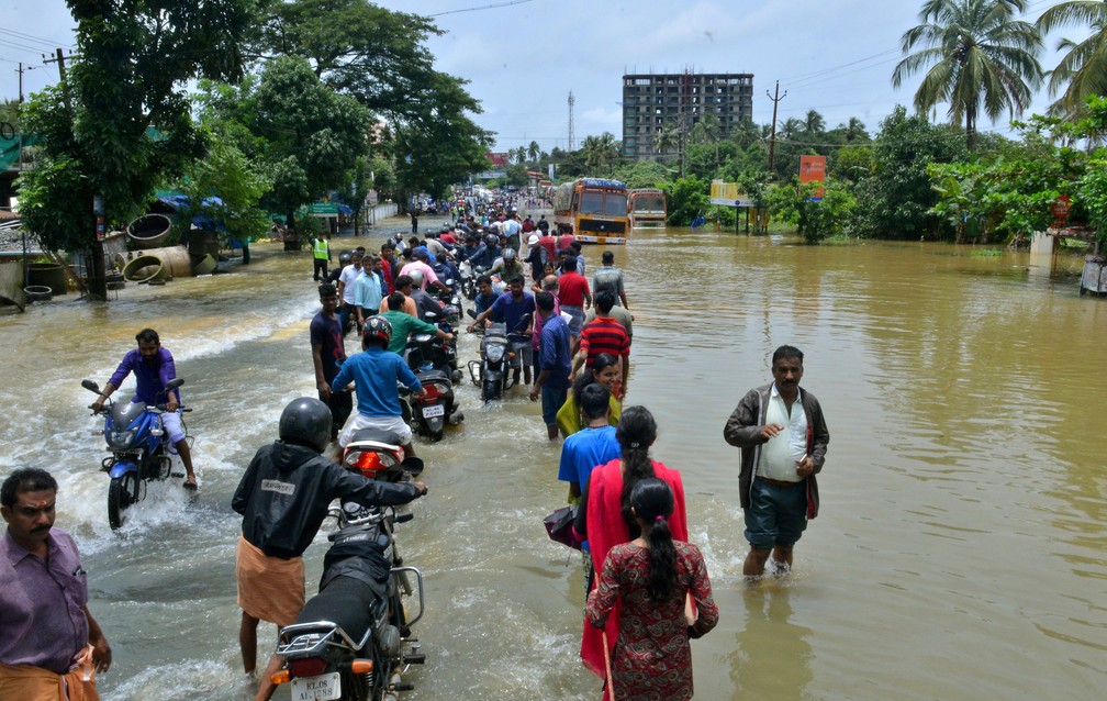 Pessoas caminham pela água durante inundação em Thrissur, em Kerala, no sul da Índia, nesta sexta-feira (17)  (Foto: Associated Press)
